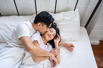 Obraz na płótnie Canvas Asian husband kissing his wife while lying down sleep on bed in bedroom. 