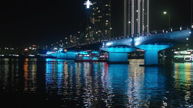 Cinematic night view of Tran Thi Ly Bridge over Han river and cruise sailing in Da Nang City of Vietnam illuminated with lights