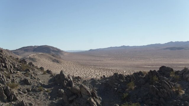 Aerial above rocky desert ledges and peaks overlooking dry lakebed in Johnson Valley, California at sunset
