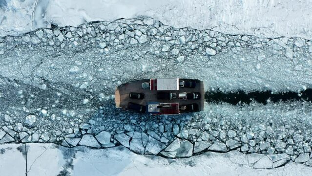 Car ferry transporting vehicles through broken frozen lake ice sheet path, aerial top down