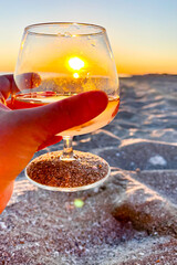 The sun in a cognac glass on the beach. Hand with a glass at sunset.