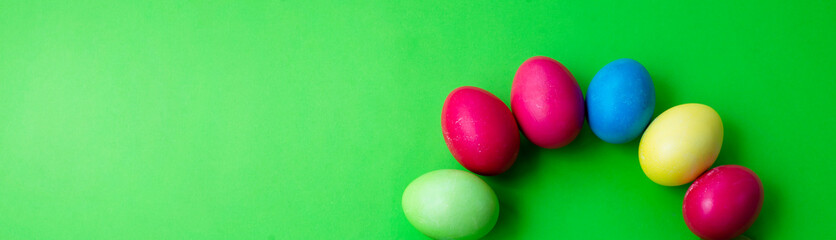 Green background and colored Easter eggs in the form of a rainbow. Copy space for text.