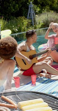 Vertical video of happy diverse friends playing guitar at pool party