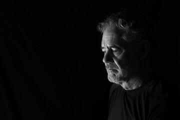 Black and white portrait of an attractive older Caucasian man with grey hair and beard. Turned to the right side, looking downward, with a thoughtful or pensive expression.  Room for copy.