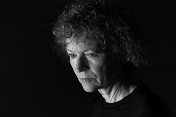 Black and white portrait of a middle aged woman with a neutral expression, looking downward.  Low key background.