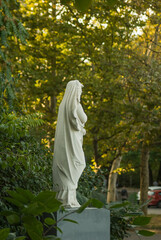 Marble statue of a grieving saint in a park surrounded by trees