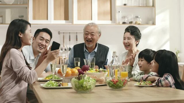 happy three generational asian family sitting at dining table at home enjoying meal together