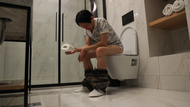 Asian Youngman  feeling stressed as holds a roll of toilet paper Going to the bathroom toilet room