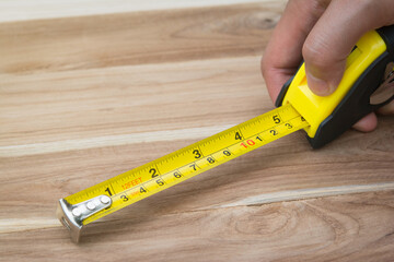 Female hand holding tape measure on wooden background, carpenter, measure the length of wooden.