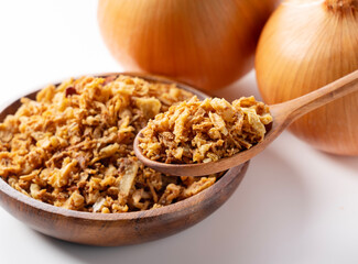 Fried onions and wooden spoon in bowl on white background.