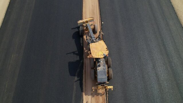 Road construction grader top view. Aerial shot. Construction grader levels the ground between an asphalt road for further installation of road fenders. Road construction works. Heavy machinery