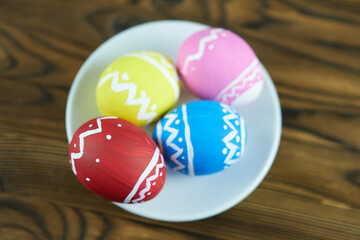 Fototapeta na wymiar Colorful Easter eggs on a white saucer, wooden background. Easter background.