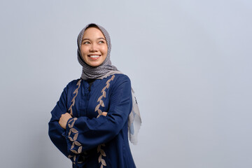 Smiling young Asian Muslim woman with arms crossed and looking away to copy space isolated over white background