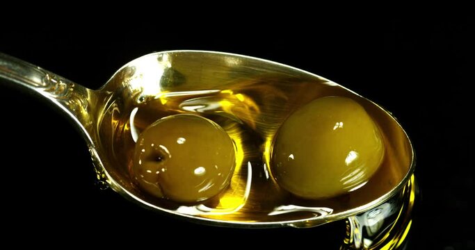 Green Olive, Olea europaea, Falling in a Spoon against Black Background, Slow Motion 4K