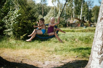 cute little boy and girl having fun on a spiderweb tree swing at playground. Summer vacation in the nature.