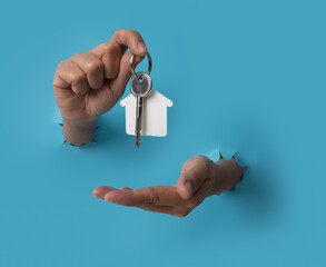 Female hand holding house key breaks through blue paper background.