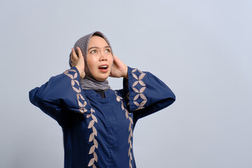 Angry young Asian Muslim woman screaming covering ears with both hands, distressed by noise isolated over white background