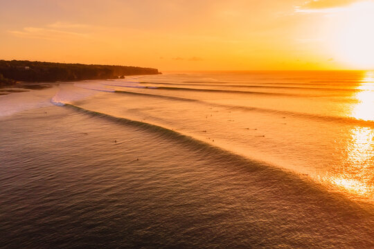 Aerial view of surfing waves at bright sunset. Perfect swell in Bali