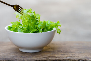A fork that picks up salad from a white bowl on a wooden background. Healthy food concept.