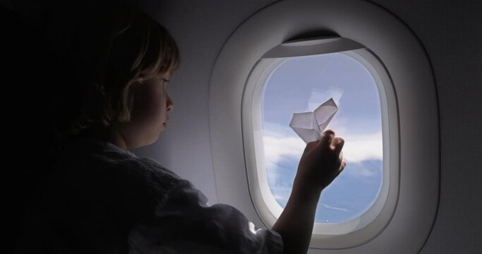 The boy on the plane is playing with a paper airplane, origami in the form of an airplane. A child dreamily plays with a paper airplane, planning to become a steward in the future and fly airplanes.