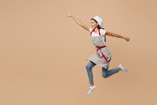 Full body side profile view young housewife housekeeper chef baker latin woman wear apron toque hat do super hero gesture pov flying isolated on plain pastel light beige background. Cook food concept.