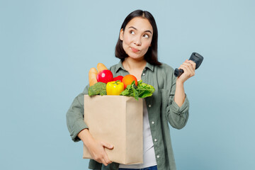 Fototapeta na wymiar Young pensive happy woman wears casual clothes hold brown paper bag scanning food products check bar code isolated on plain blue background studio portrait. Delivery service from shop or restaurant.