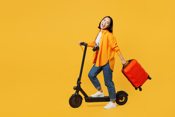 Young woman wear summer casual clothes hold suitcase riding electric scooter isolated on plain yellow background. Tourist travel abroad in free spare time rest getaway Air flight trip journey concept