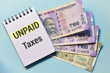 Notepad with the inscription Unpaid Taxes with Indian currency banknotes on color background. 