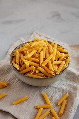 Raw Organic Penne Pasta in a Bowl on a gray background, side view..