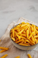 Raw Organic Penne Pasta in a Bowl on a gray background, side view.
