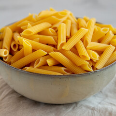 Raw Organic Penne Pasta in a Bowl on a gray background, side view. Close-up.