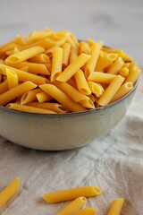 Raw Organic Penne Pasta in a Bowl on a gray background, side view. Close-up.