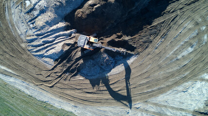 Aerial shot of a working excavator with long shadow on construction site. Top down view from drone.