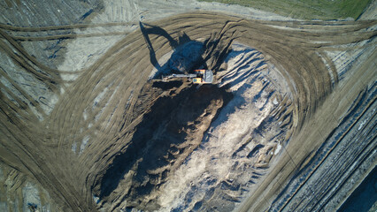 Aerial shot of a working excavator with long shadow on construction site. Top down view from drone.