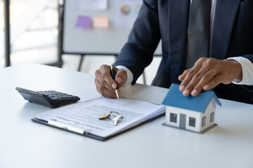 Young Asian businessman explaining and pointing to the elements of the model house model and...