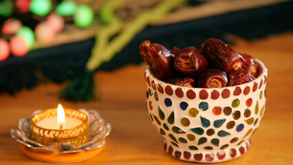 Big dates eaten during Ramadan being dropped in a designer bowl - Muslim festival. Closeup shot of a brightly burning Diya and rosary beads together on the occasion of Eid