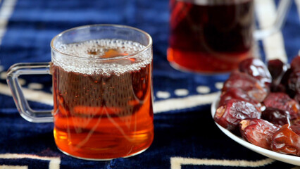 A glass of healthy and tasty Arabic tea served during Ramadan - Eid celebrations. Closeup shot of a colorful beverage and Khajoor kept together on a blue mat - Muslim festival