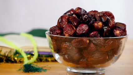 Hands keeping a delicious date / Khajoor in a glass bowl on the occasion of Eid. Holy book of Quran and colorful prayer beads kept together on a wooden table against a white background