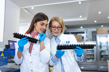 Two scientists are working in laboratory. Young female researcher and her senior supervisor are doing investigations with test tubes.