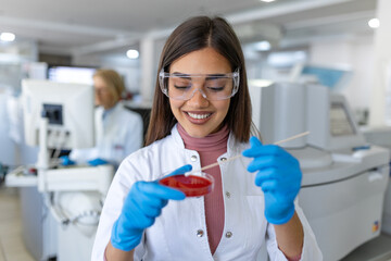 Petri dish in hand of young scientist near microscope in laboratory. Bacterial culture plate...