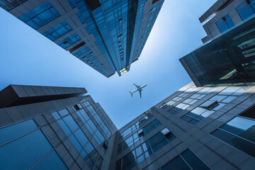Fototapeta na wymiar Tall city buildings and a plane flying overhead.