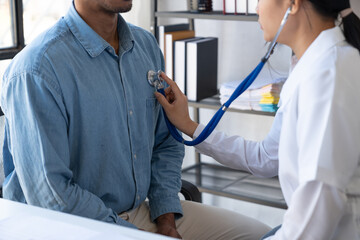 An Asian female doctor uses a stethoscope to listen to the heartbeat of a male patient for guidance in treatment and preventive care. health check concept.
