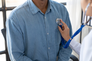 An Asian female doctor uses a stethoscope to listen to the heartbeat of a male patient for guidance in treatment and preventive care. health check concept. © Phimwilai