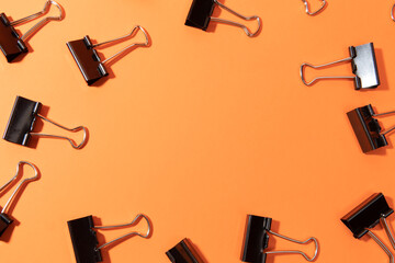 Black binder clips on orange background, flat lay. Space for text