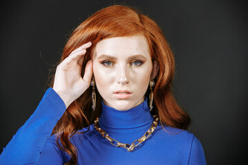 Model with red hair in blue clothes with bright make-up on a dark background