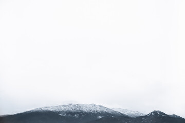 Fototapeta na wymiar Snow storm in the mountains. Dark silhouette of peaks on a white background in a haze