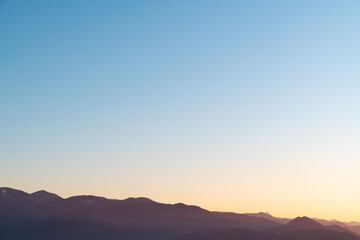 Hazy misty burgundy mountain silhouettes with aerial perspective against a sundown sky. Soft blue and yellow gradient