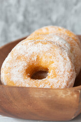 Ring doughnuts, or donuts, in a brown wooden dish bowl.  With a grey concrete background