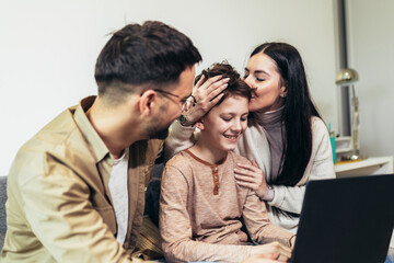 Cheerful Caucasian parents and their little boy using laptop at home together, watching movie or browsing internet