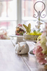 A little blonde girl in a yellow dress is sitting at a festive Easter table with rabbits.A baby and a rabbit. The concept of Easter.Easter at the table. The Christian tradition.